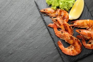 Delicious seafood dish. Tasty grilled shrimps with lemon and lettuce on black table, flat lay. Space for text