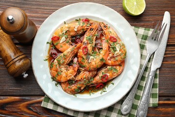 Tasty grilled shrimps with spices, sauce and cutlery on wooden table, flat lay. Delicious seafood dish