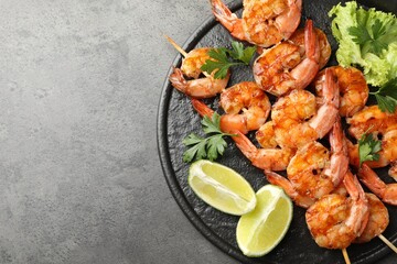 Skewers with tasty grilled shrimps, lime slices, parsley and lettuce on grey table, top view with space for text. Delicious seafood dish