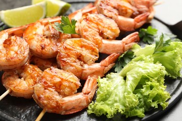 Skewers with tasty grilled shrimps, lime slices, parsley and lettuce on grey table, closeup. Delicious seafood dish