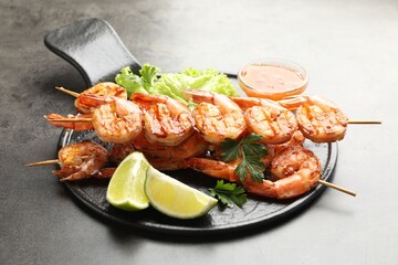 Skewers with tasty grilled shrimps, lime slices, parsley, lettuce and sauce on grey table. Delicious seafood dish