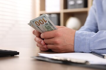 Man counting dollar banknotes at table, closeup