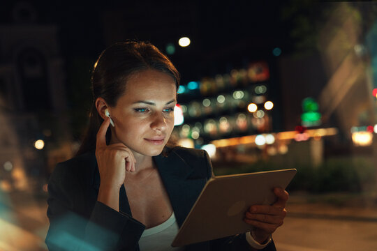 Female using digital tablet with earbuds outdoors in urban evening
