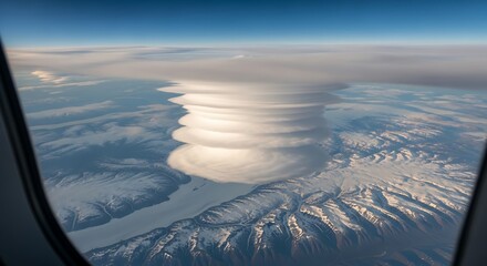 Volcanic eruption ash cloud seen from an airplane window over snowy mountains.