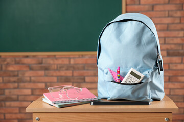 Light blue backpack with different stationery and glasses on desk in classroom