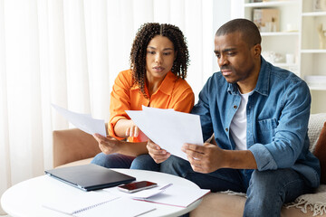 Focused African American couple working on finances at home, reading documents and planning expenses. Concept of teamwork, partnership, budgeting, lifestyle and money