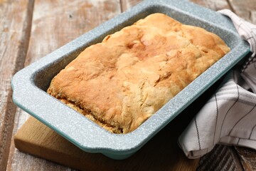 Freshly baked cornbread in baking dish and napkin on color wooden table, closeup