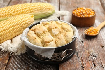 Freshly baked cornbread in cake pan, cobs and napkin on color wooden table, closeup