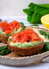 Bruschetta with smoked trout fish and avocado cream on bread served on the ceramic plate with lemon and herbs