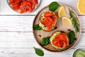 Bruschetta with smoked trout fish and avocado cream on bread served on the ceramic plate with lemon and herbs. Top view