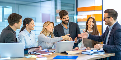 Business team leader woman is welcoming new team member with handshake while colleagues are excitedly watching during office meeting