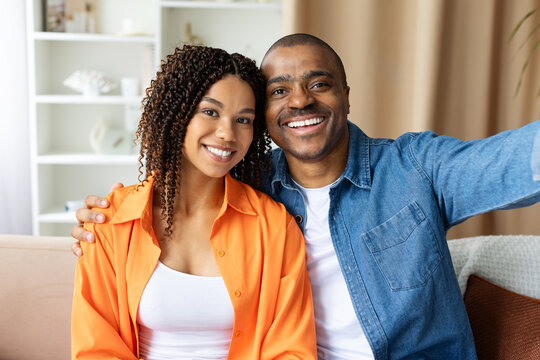Smiling African American couple taking selfie at home, looking at camera with happiness. Concept of modern love, lifestyle, family bonding, joy and togetherness