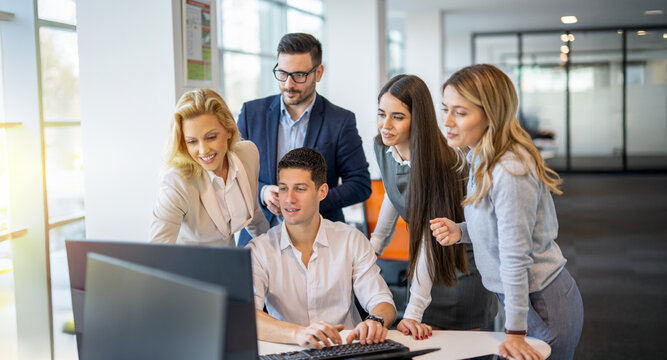 Business people gathered around young colleague at computer discussing potential development results and generating ideas together