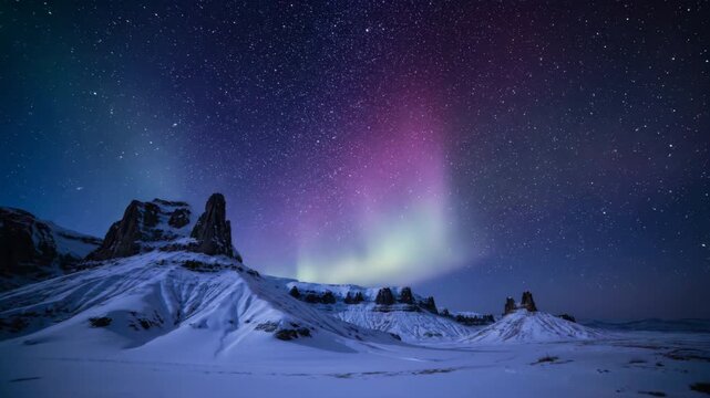 A moody time-lapse reveals the slow ebb and flow of a deep blue and crimson aurora over ancient, snow-dusted rock formations ice, red light, southern lights