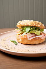 Bagel sandwich showcasing fresh prosciutto, creamy avocado, and vibrant arugula on a sesame seed bun