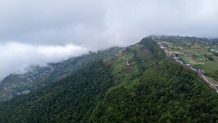 Aerial of Village in rain cloud cover tropical green mountain. Rainy season. Misty cover green forest. beautiful green village