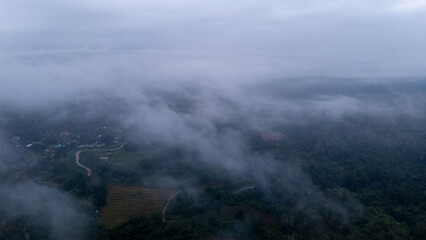 Aerial of Village in rain cloud cover tropical green mountain. Rainy season. Misty cover green forest. beautiful green village