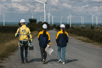 Group of engineers walking through wind farm with safety gear, toolbox, and blueprints, symbolizing teamwork, field inspection, and collaboration in the renewable energy and clean power industry.