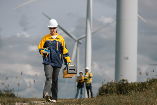 Female engineer walking at a wind farm with safety equipment and toolbox, symbolizing renewable energy maintenance, green technology, and professional field inspection for sustainable energy systems.
