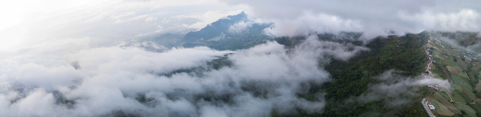 Aerial of Village in rain cloud cover tropical green mountain. Rainy season. Misty cover green forest. beautiful green village