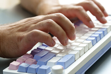 Hands typing on a colorful keyboard in a modern workspace setting during daylight hours