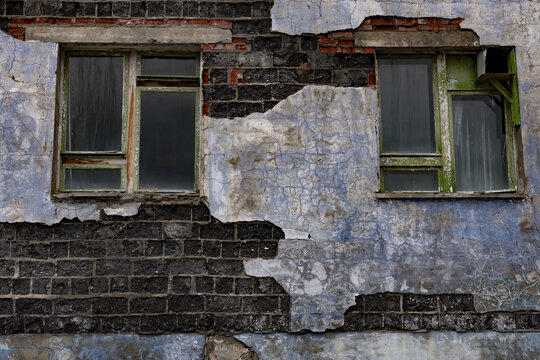 View of crumbling brickwork revealing layers of blue paint and faded green window frames on a weathered wall, Pyramiden, Svalbard and Jan Mayen.