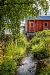 Traditionel red Norwegian housr besides a creek