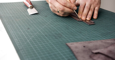 Close-up of craftsman marking leather with ruler and awl for handmade leatherwork