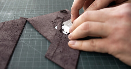 Leatherworker skiving edge of brown leather piece with blade tool