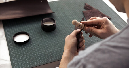 Leather artisan burnishing edge of leather piece with wooden slicker tool