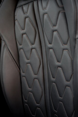 Car leather seat with brown-bronze stitches - close-up view. Black leather seat in modern car - selective focus.

