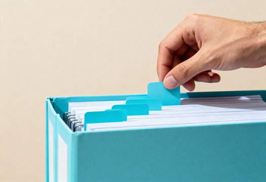 Business person organizing important documents in a large blue filing system, hand sorting through file folders in an office setting