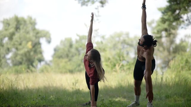 People Practicing Yoga Side Angle Pose In Forest. Sportsmen Stretching Body. Group Doing Fitness Workout In Nature