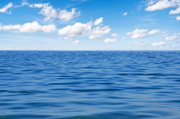 Obraz premium A wide view of the calm blue ocean stretching to the horizon under a bright sky with scattered white clouds.