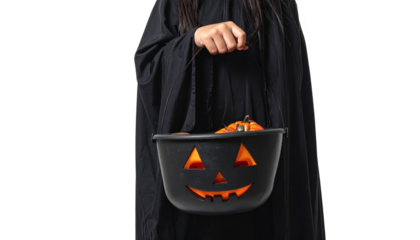 A person holding a Halloween pumpkin-shaped bucket, in a black cloak outfit, celebrating the Halloween night