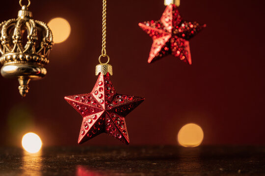 Festive red star ornaments and golden crown hanging against a blurred warm bokeh background, perfect for holiday celebrations