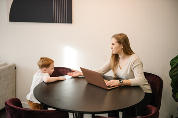 Mother working from home with kid. Quarantine and closed nursery school. Distance learning through war. Child make noise and disturb woman work. Homeschooling and freelance job. Stay at home.
