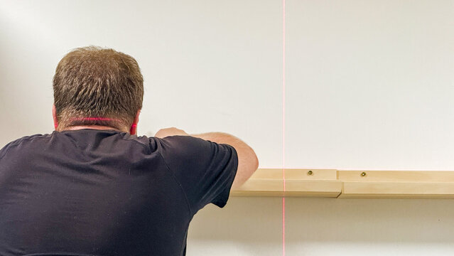 A Caucasian male diligently aligns a shelf using a laser level, embodying precision for Inventors' Day or DIY Festival