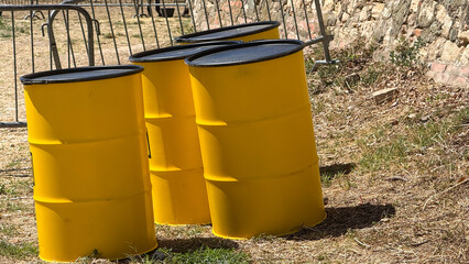 Pile of sunshine-yellow barrels basking in midday sun, evoking Earth Day cleanup vibes,...