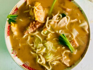 Close-up of a hot bowl of noodle soup served with vegetables, meat, and egg in a savory broth