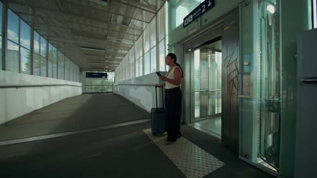 The elevator doors open and a woman comes out with a mobile phone and a suitcase in her hands.