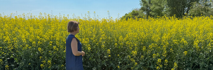 A contemplative woman of European descent stands amid dancing yellow canola blooms, celebrating Lughnasadh and the vibrant pollinators' waltz