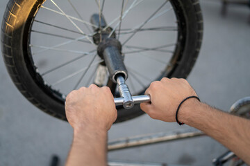 A person is focused on removing the back wheel of a BMX bike using a wrench, surrounded by parked...