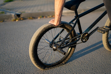 Naklejka premium A BMX bicycle rests on a city street with a flat rear tire, highlighting the punctured condition under the warm light of sunset, surrounded by urban features.