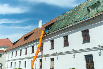 Historic buildings require careful renovation, building debris travels through an orange chute during roof repairs. Renovation of an old building. The roof is under construction.