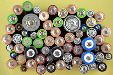 Used AA batteries and proper disposal of environmentally and soil toxic batteries on a green background.