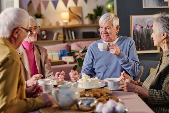 Group of senior Caucasian men and women sitting together enjoying tea and cake, engaging in conversation around table with desserts, smiling and interacting in cozy indoor setting - Powered by Adobe