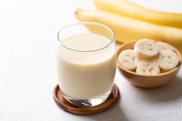 Banana milk in glass with sliced banana and fruit on white background