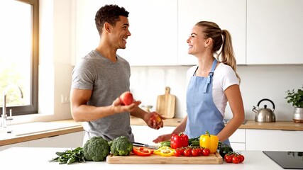 Young mixed race couple cooking and laughing in their cozy kitchen as the man playfully tosses red apples, sharing a warm, playful moment of love and healthy togetherness - Powered by Adobe