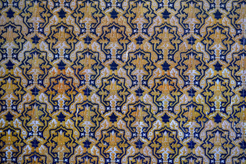 This is a detailed, close-up photo of traditional Sevillian azulejo tiles. The intricate pattern features a repeating design of yellow-orange 